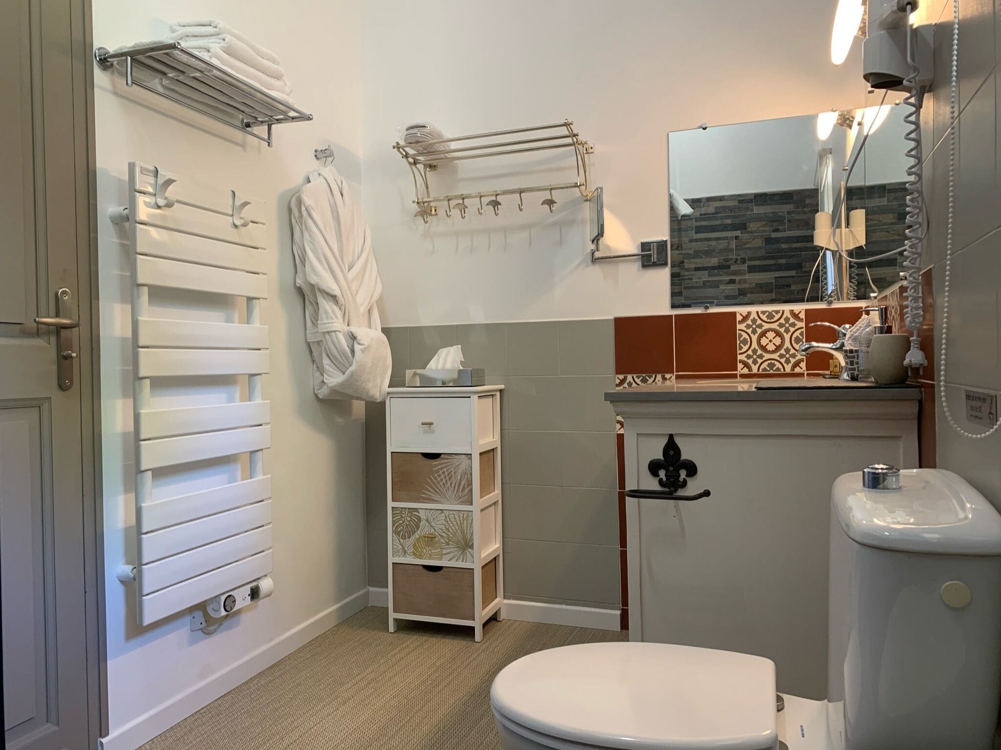 Une salle de bain comprenant des toilettes, un lavabo, un porte-serviettes, un peignoir et un espace douche.