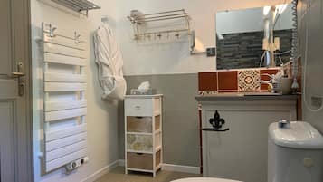 Une salle de bain comprenant des toilettes, un lavabo, un porte-serviettes, un peignoir et un espace douche.