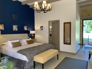 A bedroom with a large bed, a bench, a chandelier, and a door leading to a balcony. - Le Noyer Résidence (Le Bugue)