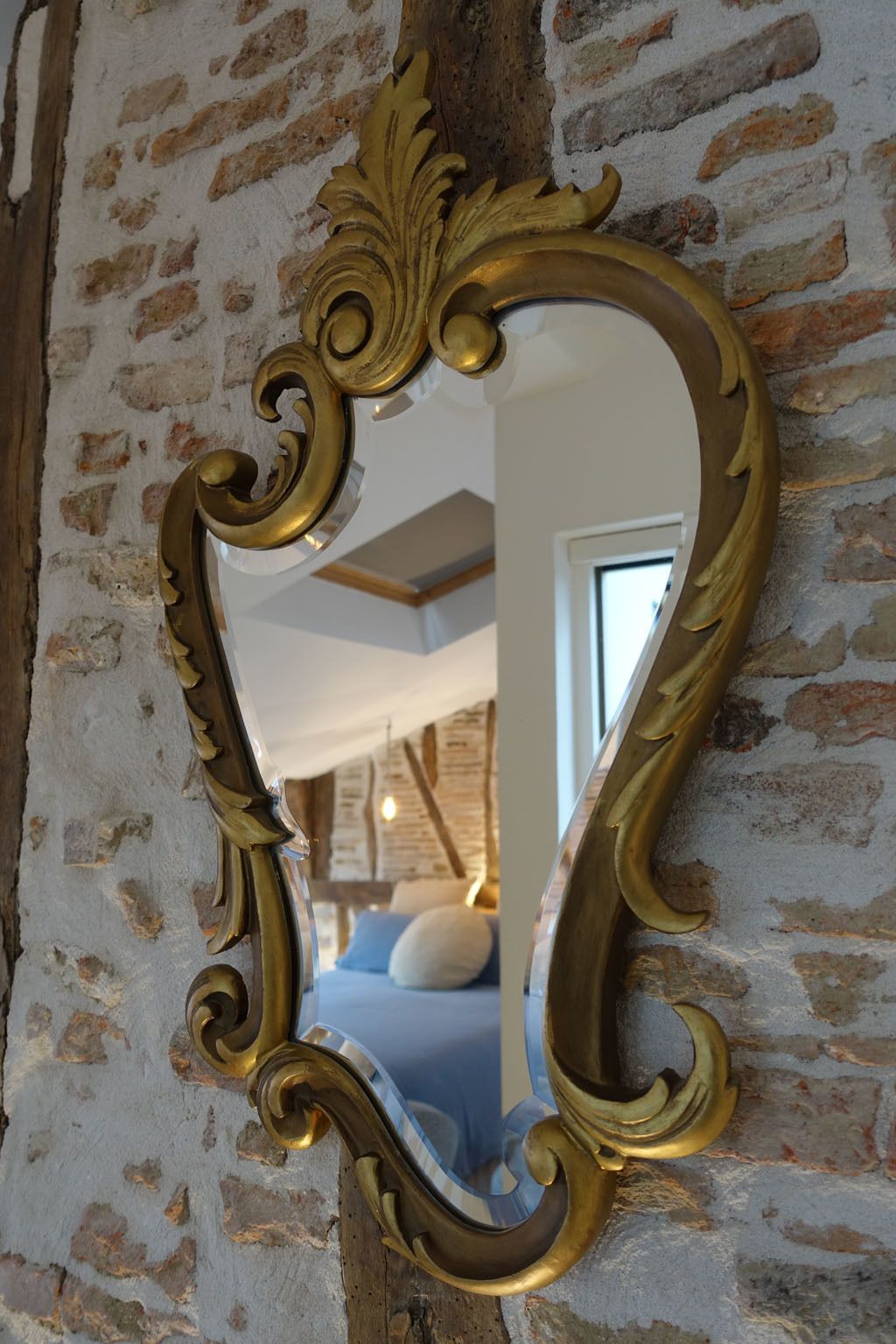 A mirror with an ornate gold frame against a brick wall.