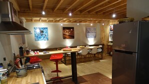 A kitchen with wooden beams, a stainless steel range hood, a refrigerator, and a dining area with chairs and a table. - Impasse du Boeuf (Lavaur)