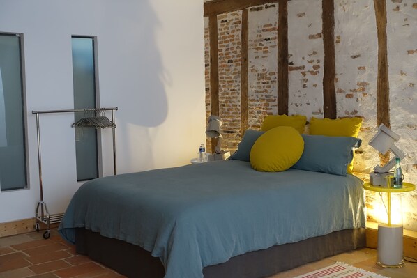 A bedroom with a bed, pillows, a bedside table, a lamp, and a water bottle. - Impasse du Boeuf (Lavaur)