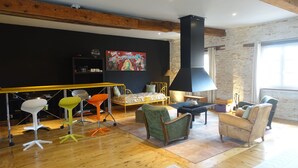 A modern living room with a wooden floor, a black wall with a colorful painting, a black chimney, and a large window. - Impasse du Boeuf (Lavaur)