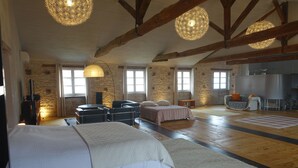 A spacious room with a large bed, a sofa, and a dining table. There are multiple windows providing natural light, and the room features exposed wooden beams and a stone wall. - Impasse du Boeuf (Lavaur)