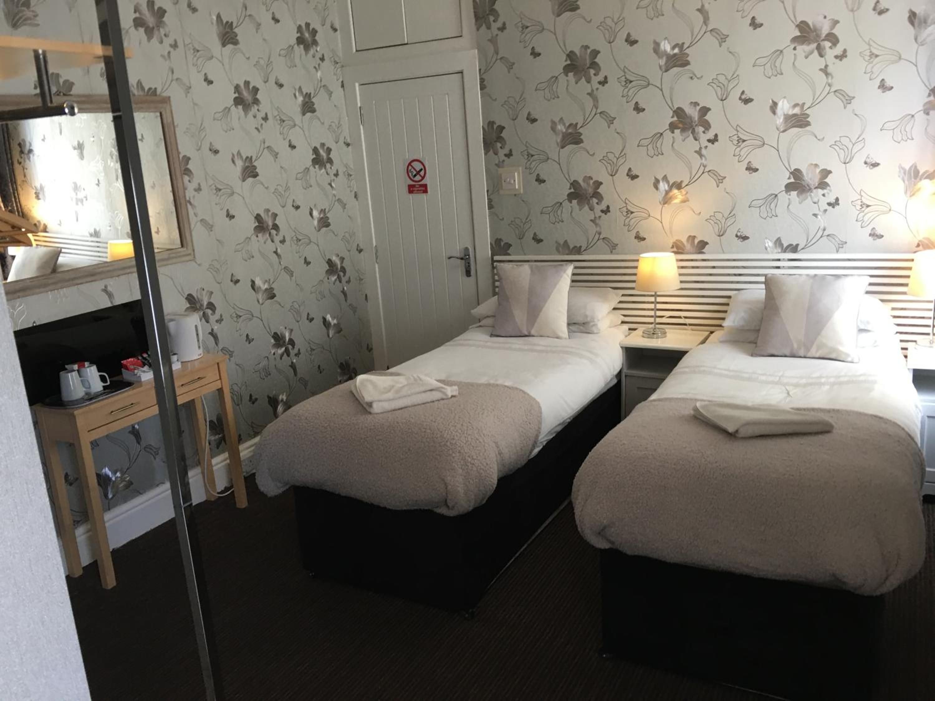A hotel room with two beds, a bedside table with a lamp, a mirror, and a wardrobe.