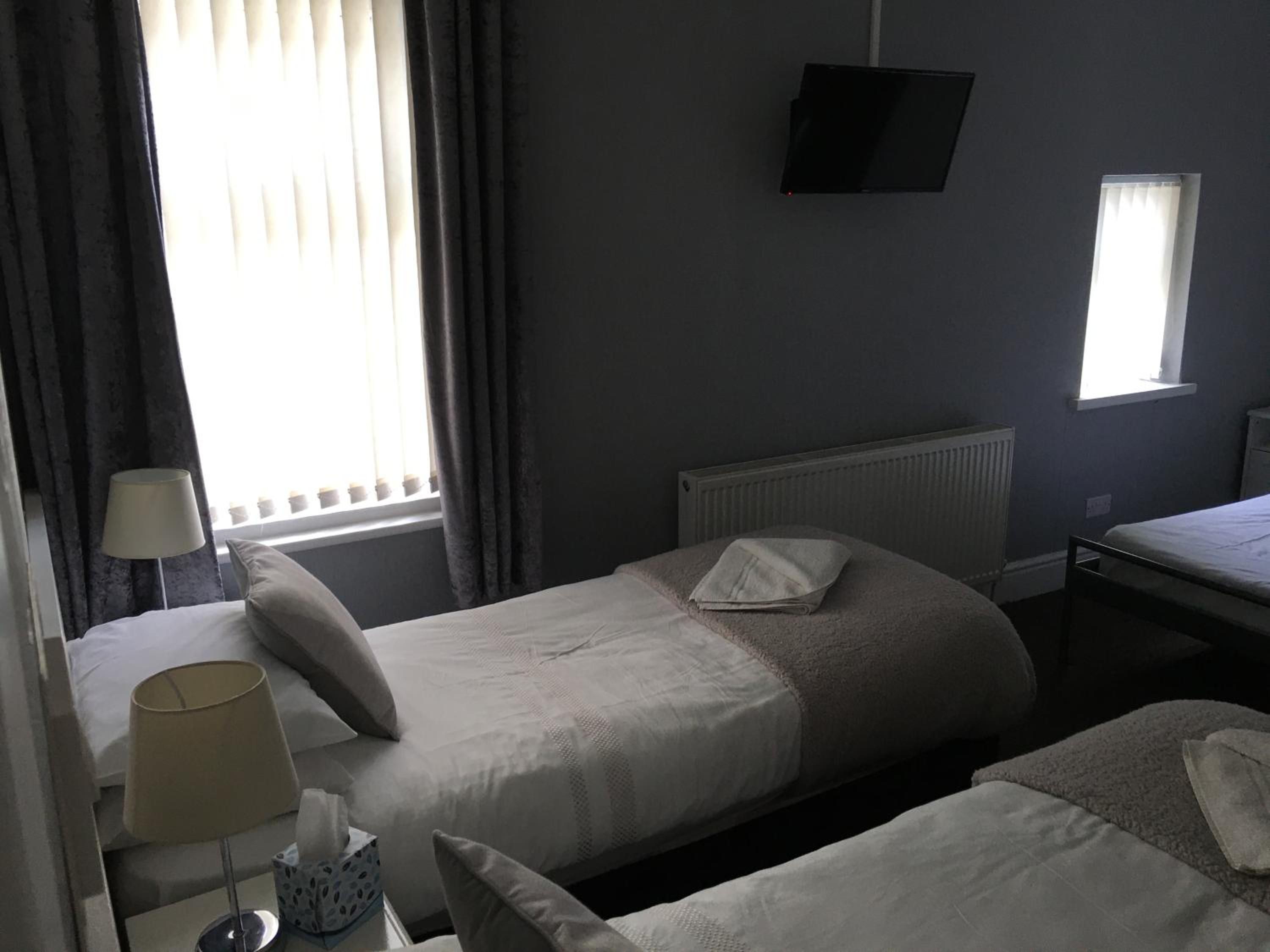 A hotel room with two beds, a TV mounted on the wall, a window with curtains, and a radiator.
