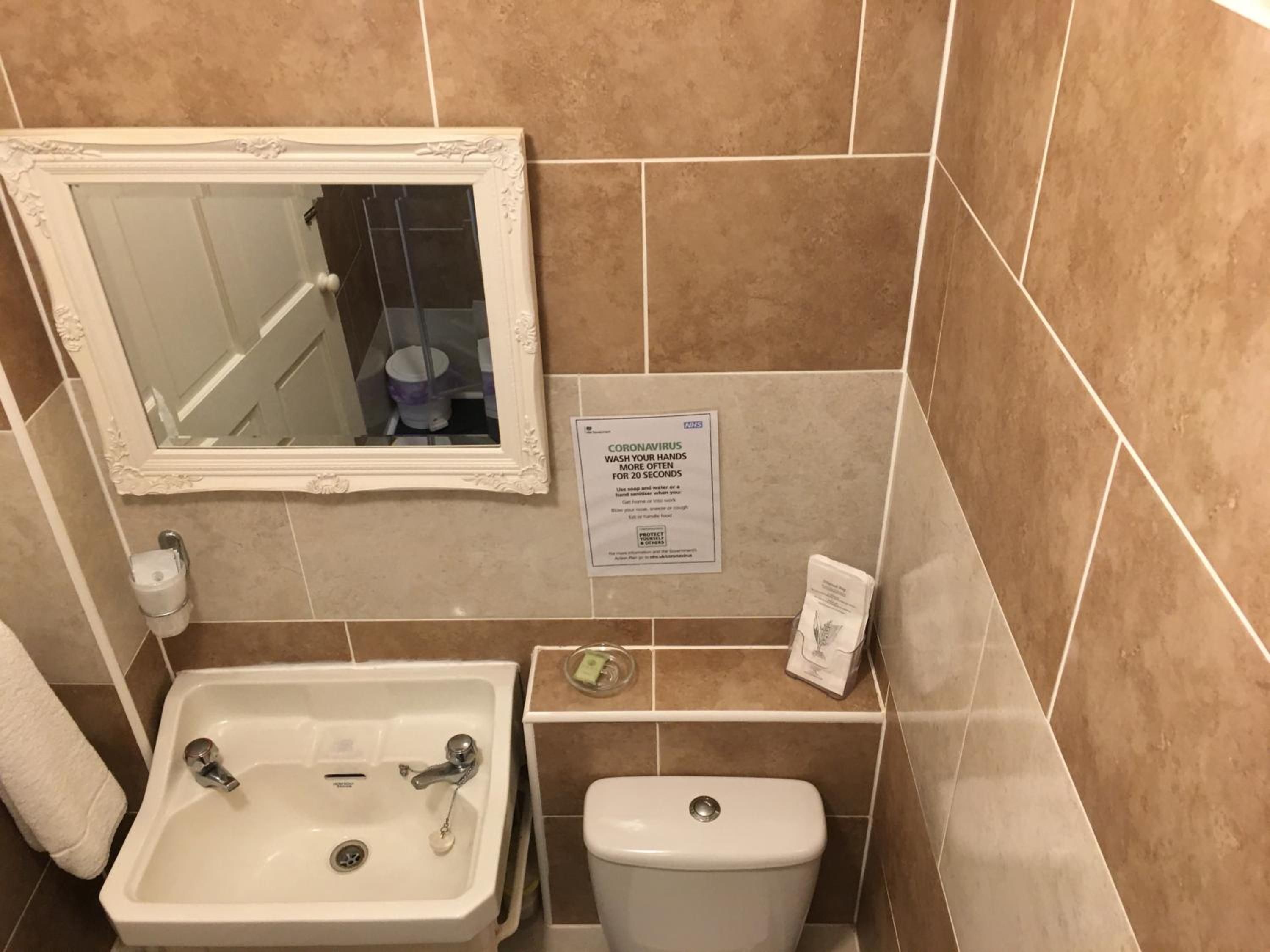 Baño con lavamanos, inodoro y espejo. Hay un cartel que recomienda lavarse las manos.