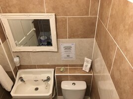 Een badkamer met een wastafel, toilet en spiegel. Er is een bordje met een advies om de handen te wassen.