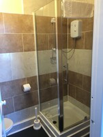 Een douchecabine met glazen wanden, een handdouche, een zeepdispenser en een toiletrolhouder aan de muur.