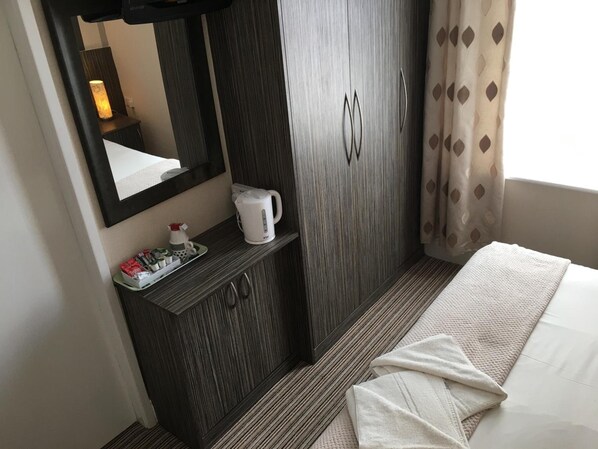 A hotel room with a bed, a bedside table with a kettle and a bottle, a wardrobe, and a mirror. - Glenheath Hotel (Blackpool)