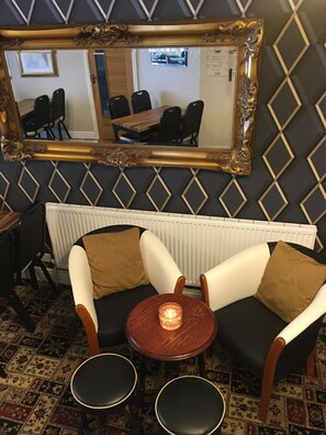 A room with a mirrored wall, a radiator, two armchairs, a small table with a candle, and a patterned carpet. - Glenheath Hotel (Blackpool)
