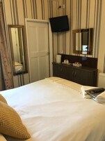 Hotellihuone, jossa on sänky, seinälle asennettu televisio, peili ja lipasto, jossa on hygieniatarvikkeita.
