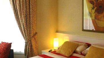 A hotel room with a bed, pillows, a nightstand, a lamp, a framed picture, and a window with curtains.