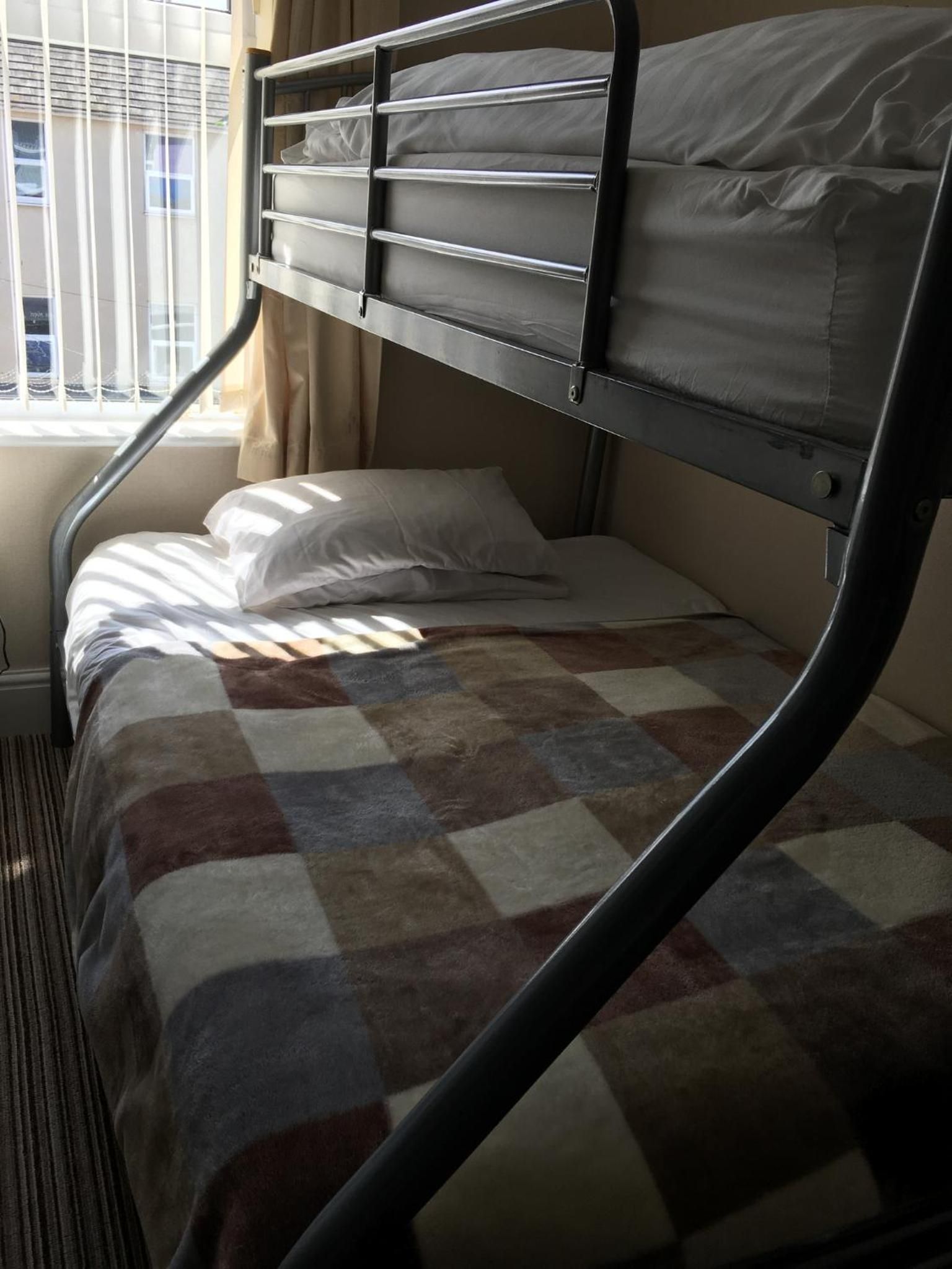 A bunk bed with a checkered blanket, a window with blinds, and a radiator.