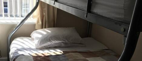 A bunk bed with a checkered blanket, a window with blinds, and a radiator.