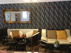 A living room with a sofa, chairs, a table, a mirror, and a patterned wall. - Glenheath Hotel (Blackpool)