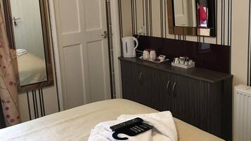 A hotel room with a bed, a TV mounted on the wall, a mirror, a dresser, and a door.