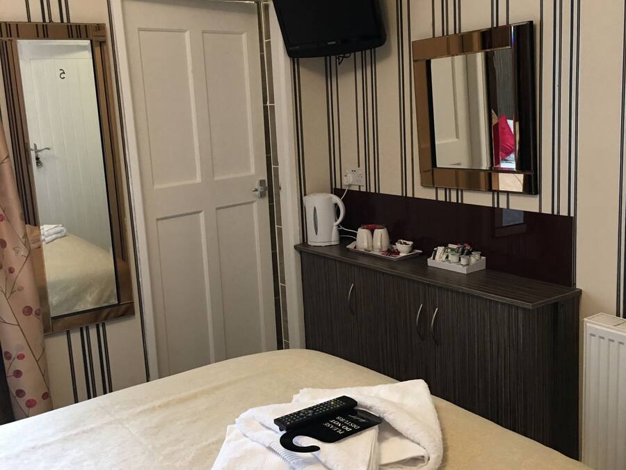 A hotel room with a bed, a TV mounted on the wall, a mirror, a dresser, and a door.