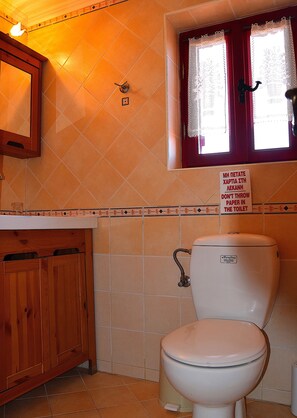 Um banheiro com vaso sanitário, um armário de madeira e janela com cortinas de renda.