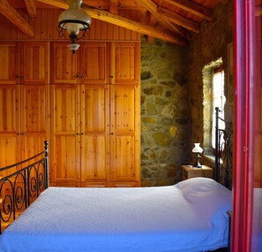 Quarto com cama de madeira, parede de pedra e guarda-roupa de madeira.