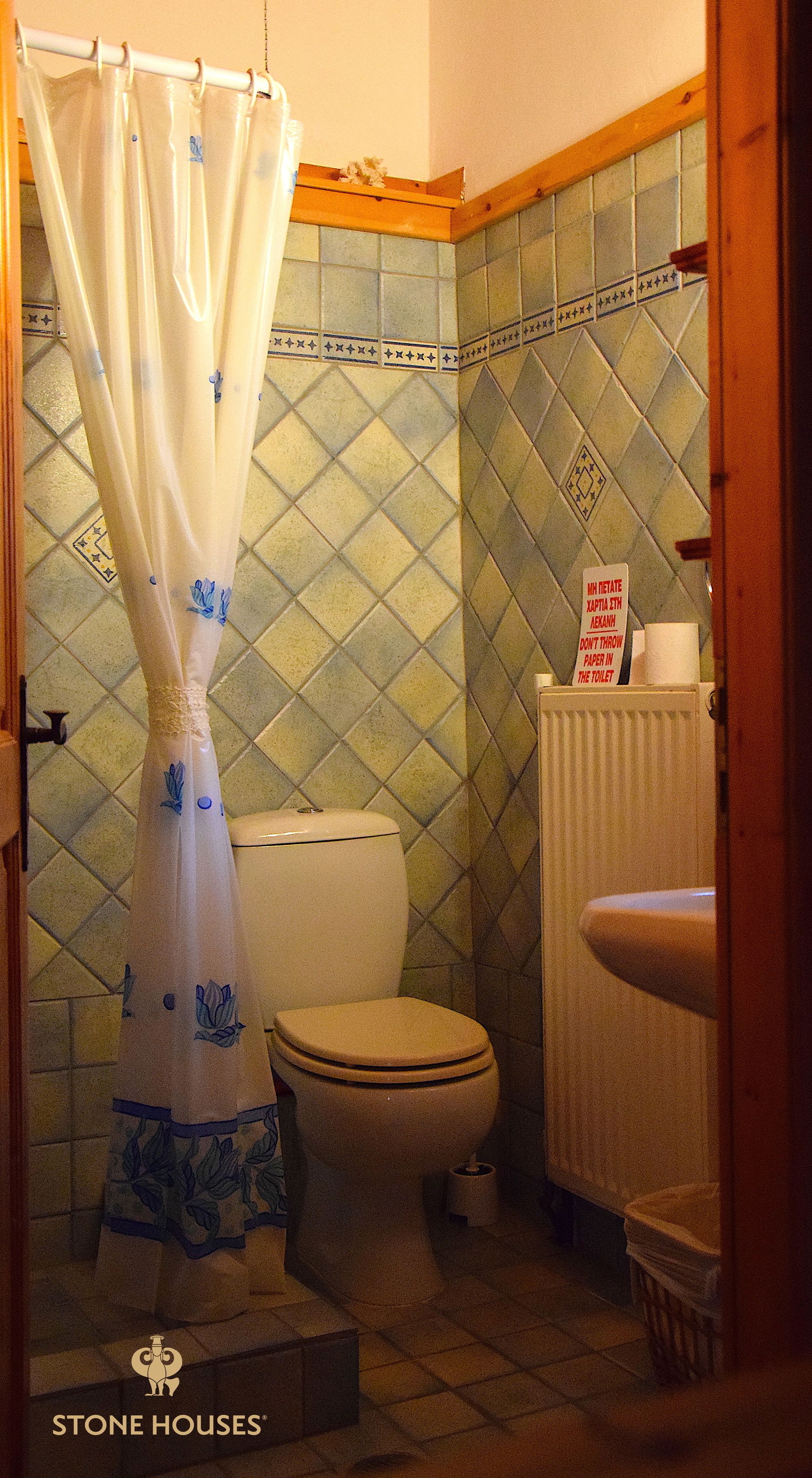 Un bagno con un water, una tenda della doccia e un cartello appeso al muro.