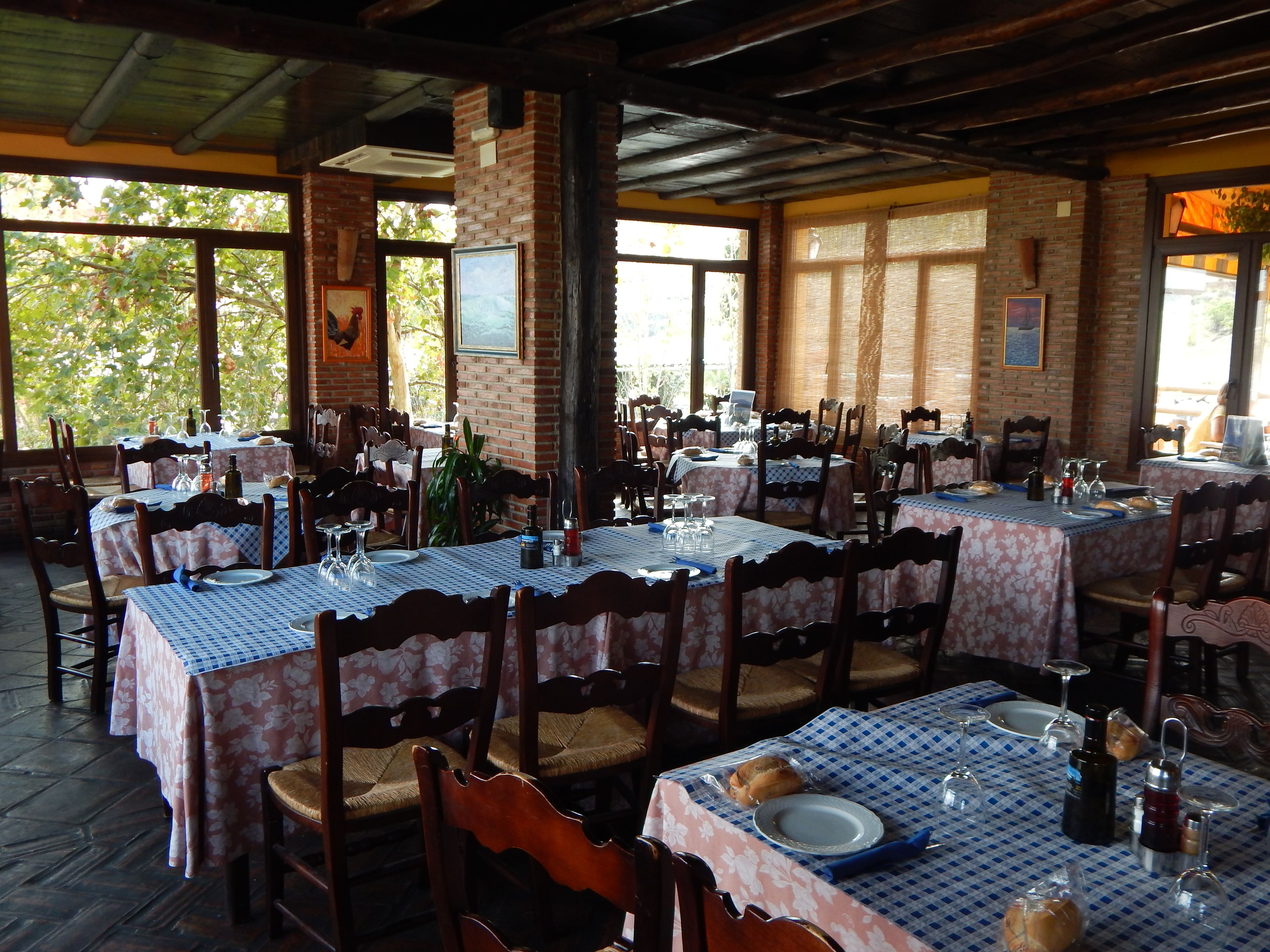 A restaurant with multiple tables, each covered with a floral tablecloth, wooden chairs, and various dining items.