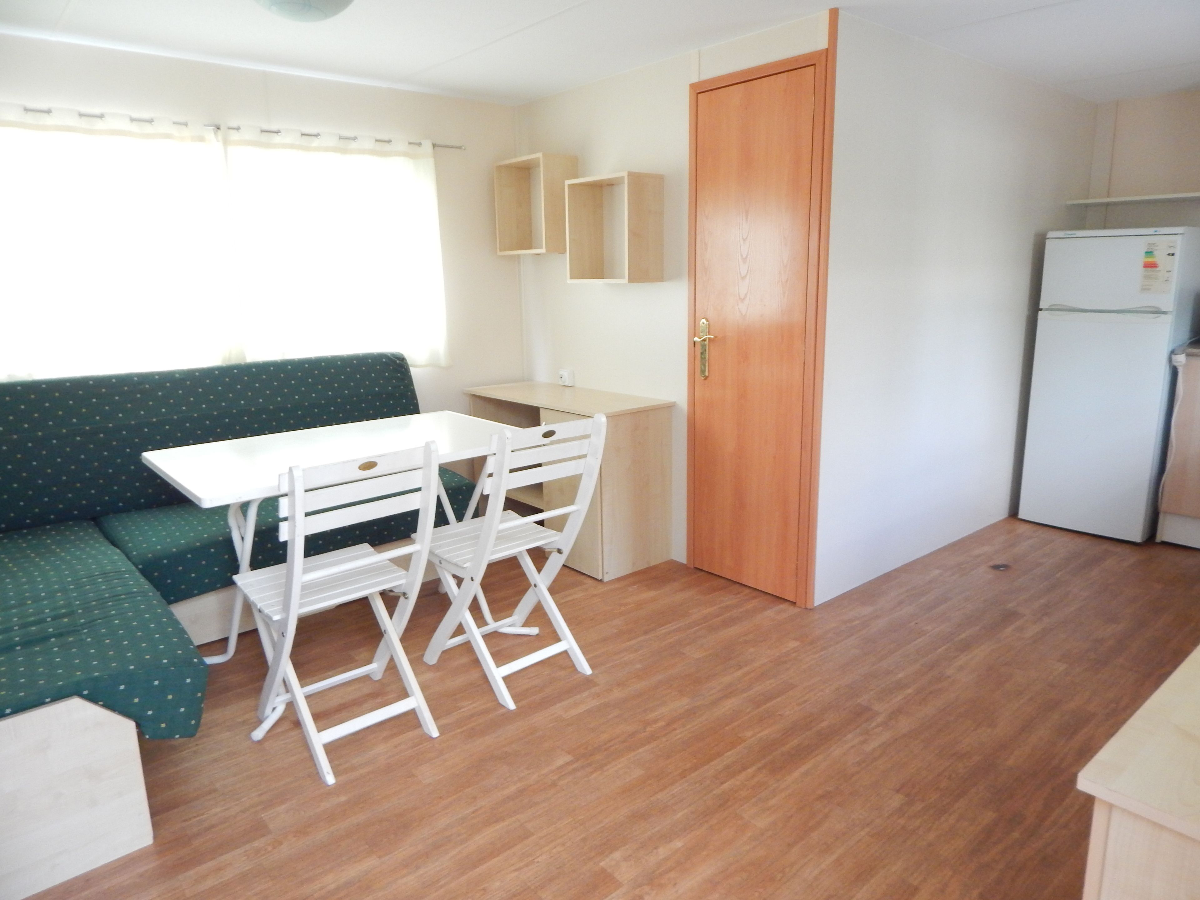 Cocina compacta con una mesa y sillas de madera, un refrigerador y un sofá verde.