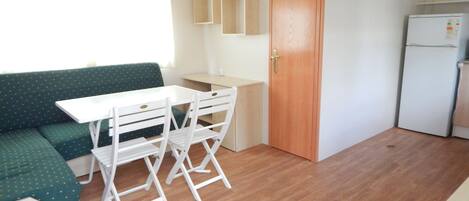 Cocina compacta con una mesa y sillas de madera, un refrigerador y un sofá verde.