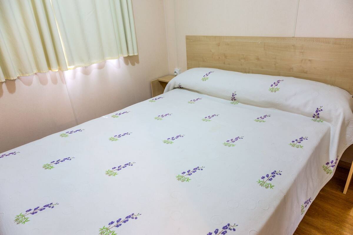 A single bed with a floral bedspread, a wooden headboard, and a nightstand with a lamp.