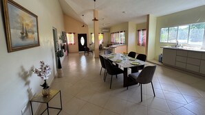 A dining area with a table set for four, a kitchen area with a window, and a hallway leading to another room. - Casa caleton (Rio San Juan)