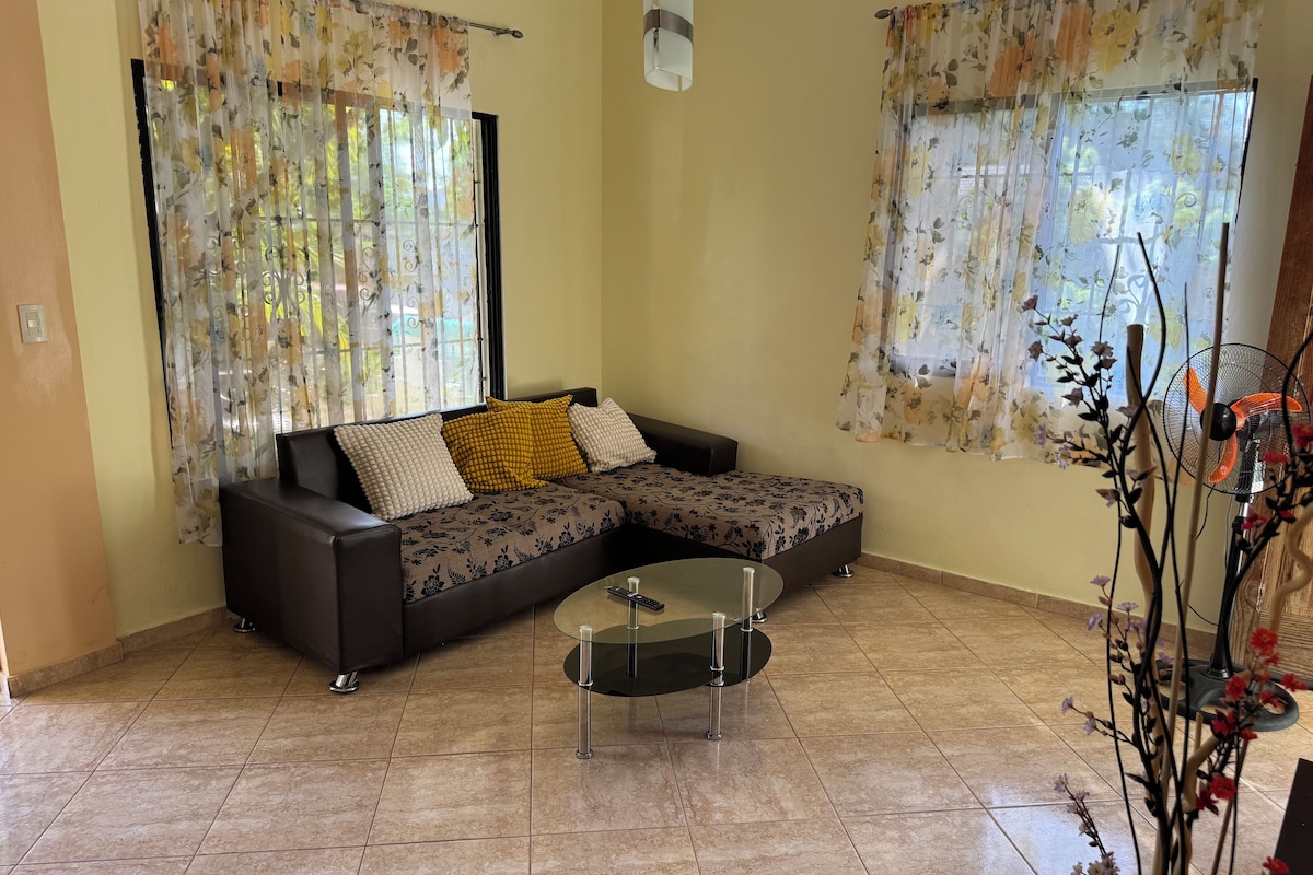A living room with a sectional sofa, a glass coffee table, and floral curtains.