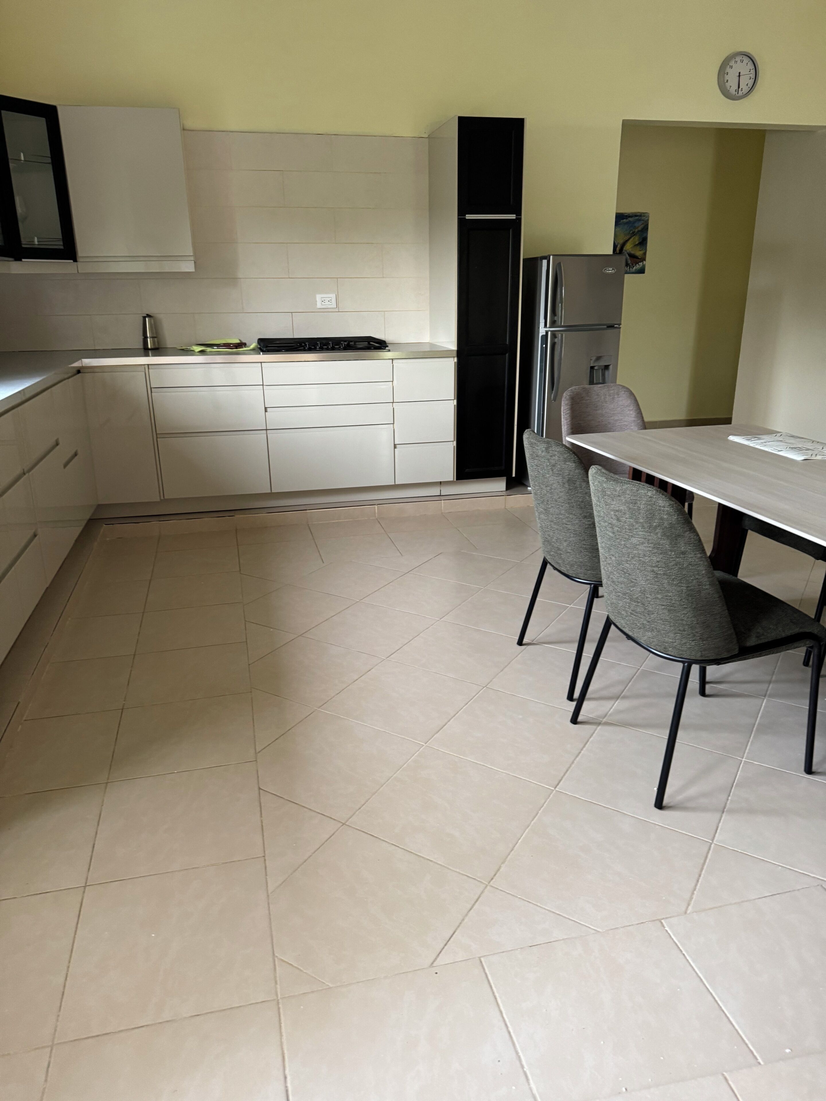 A kitchen with white cabinets, a black refrigerator, and a dining table with two chairs.
