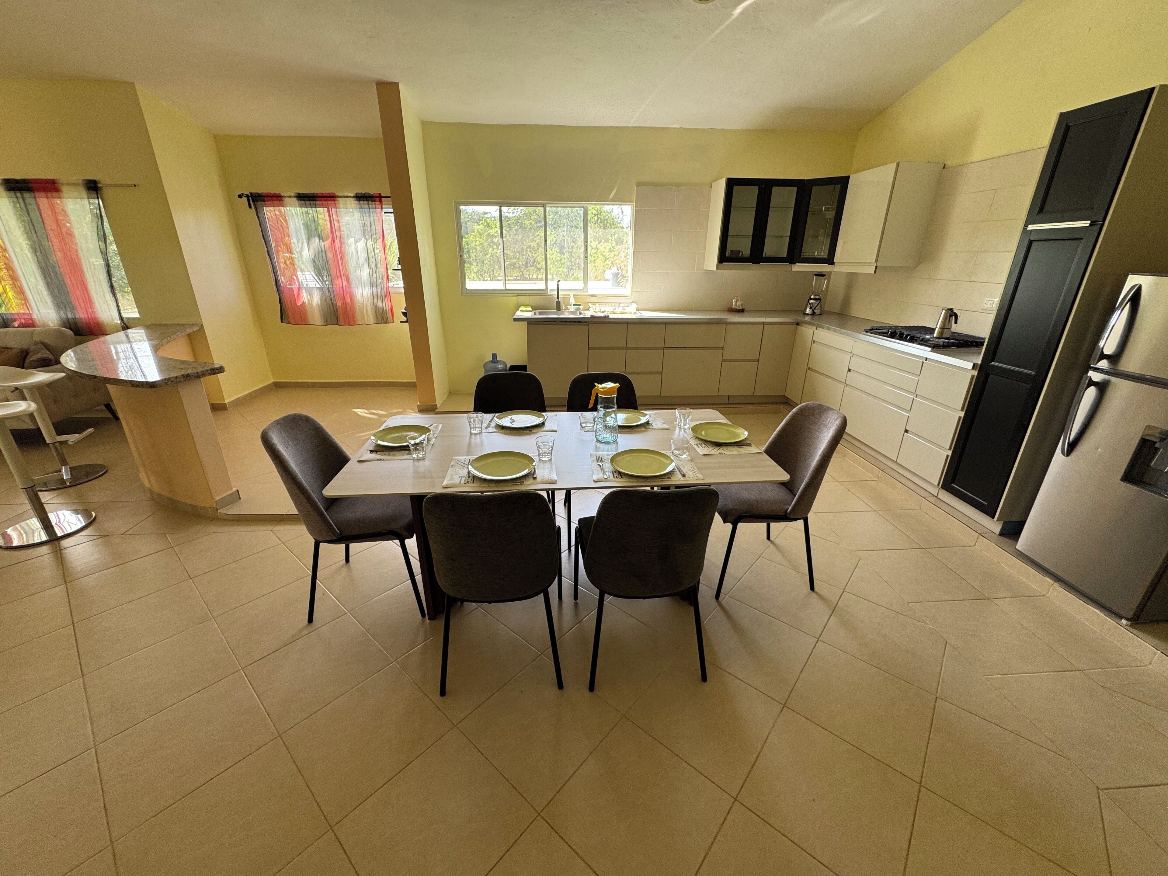 Comedor con mesa dispuesta para cuatro, cocina con electrodomésticos modernos y ventana que proporciona luz natural.