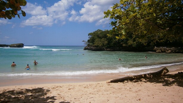 A beach with clear turquoise water, a sandy shore, and a rocky outcrop in the distance. - Casa caleton (Rio San Juan)