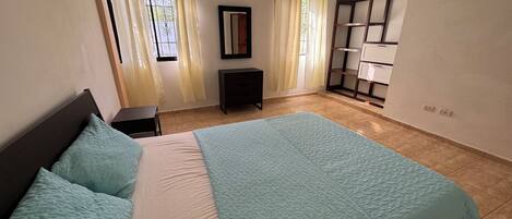 Un dormitorio con cama, mesita de noche, cómoda, espejo y ventana con cortinas.