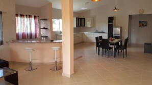 A modern kitchen with white cabinets, a dining area with a table and chairs, and a bar area with stools. - Casa caleton (Rio San Juan)