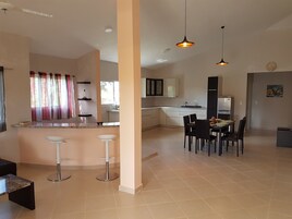 Cozinha moderna com armários brancos, área de jantar com mesa e cadeiras, e bancada com banquetas.