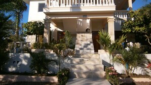 A two-story house with a balcony, a staircase leading to the entrance, and surrounding greenery. - Casa caleton (Rio San Juan)