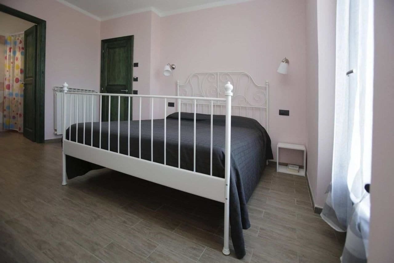 A bedroom with a white metal bed frame, a dark-colored bedspread, and a small bedside table with a lamp.