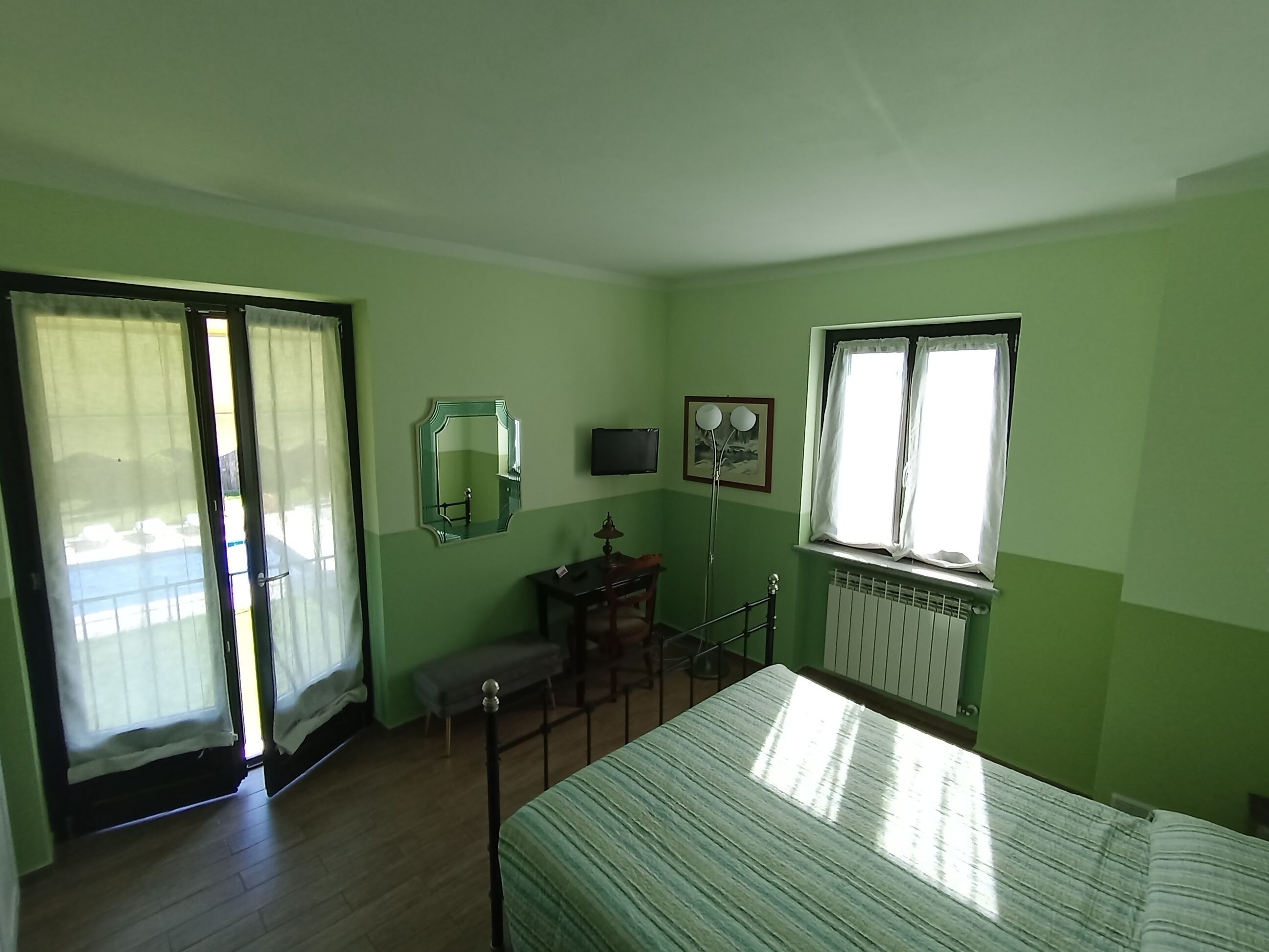 A room with a bed, a desk, a chair, a mirror, a window, and a radiator.
