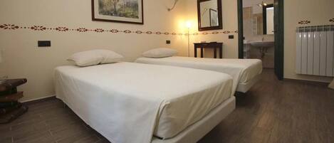 A hotel room with two beds, a bedside table, a lamp, a mirror, and a bathroom visible through an open door.