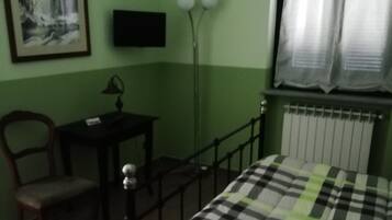 Een kamer met een bed, een bureau, een stoel, een vloerlamp en een raam met gordijnen.
