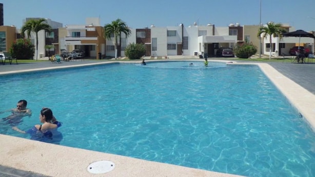 A swimming pool surrounded by modern buildings, with people swimming and lounging. - Casa Villa R (Mazatlán)