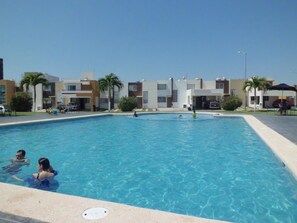 A swimming pool surrounded by modern buildings, with people swimming and lounging. - Casa Villa R (Mazatlán)