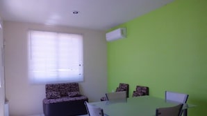 A dining area with a green wall, a window with blinds, a sofa, and a table with chairs. - Casa Villa R (Mazatlán)