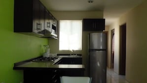 A compact kitchen with a gas stove, a refrigerator, and dark cabinets. - Casa Villa R (Mazatlán)