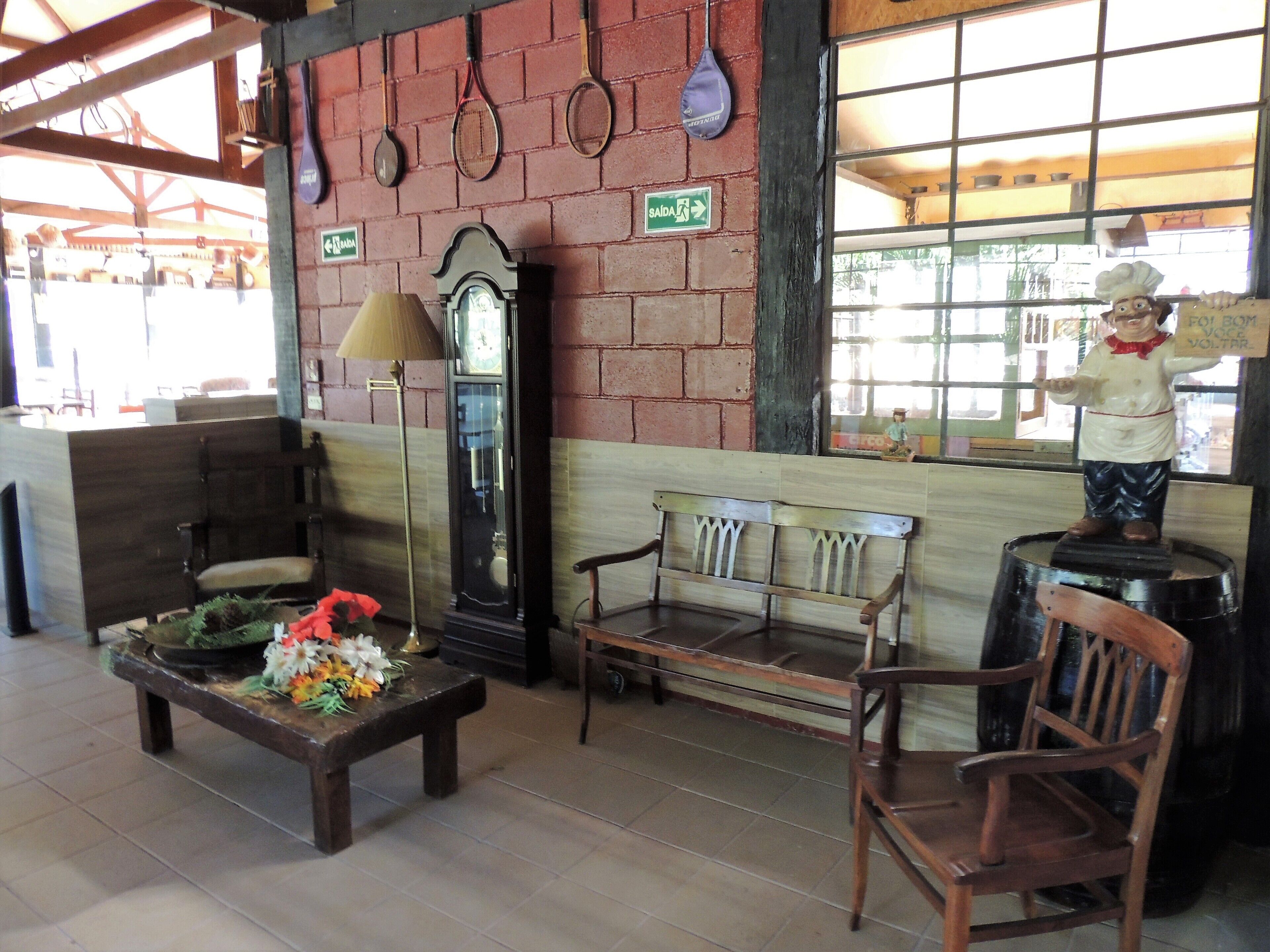 Um interior acolhedor com um banco de madeira, uma mesa com flores, um relógio de parede e uma estátua.