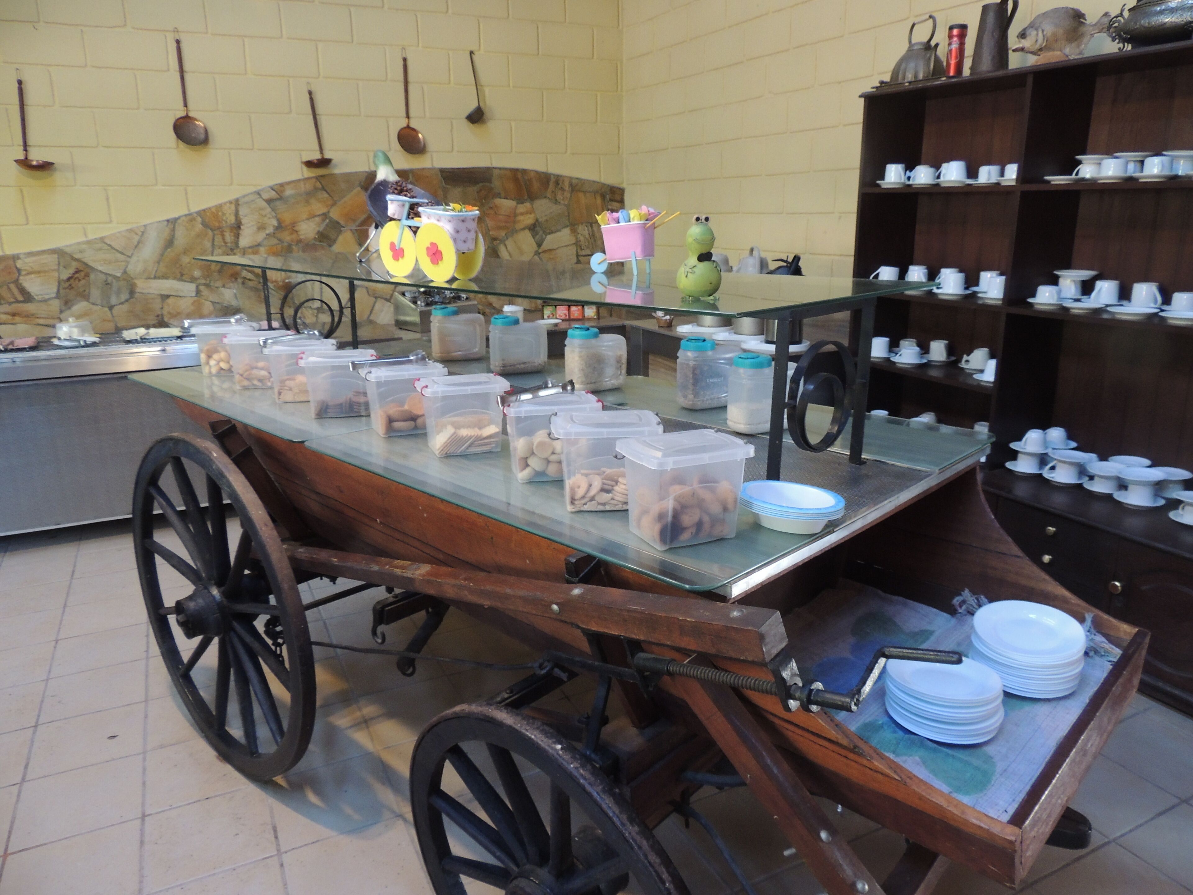 A buffet setup with a cart filled with food containers, a glass display case, and a shelf with dishes.