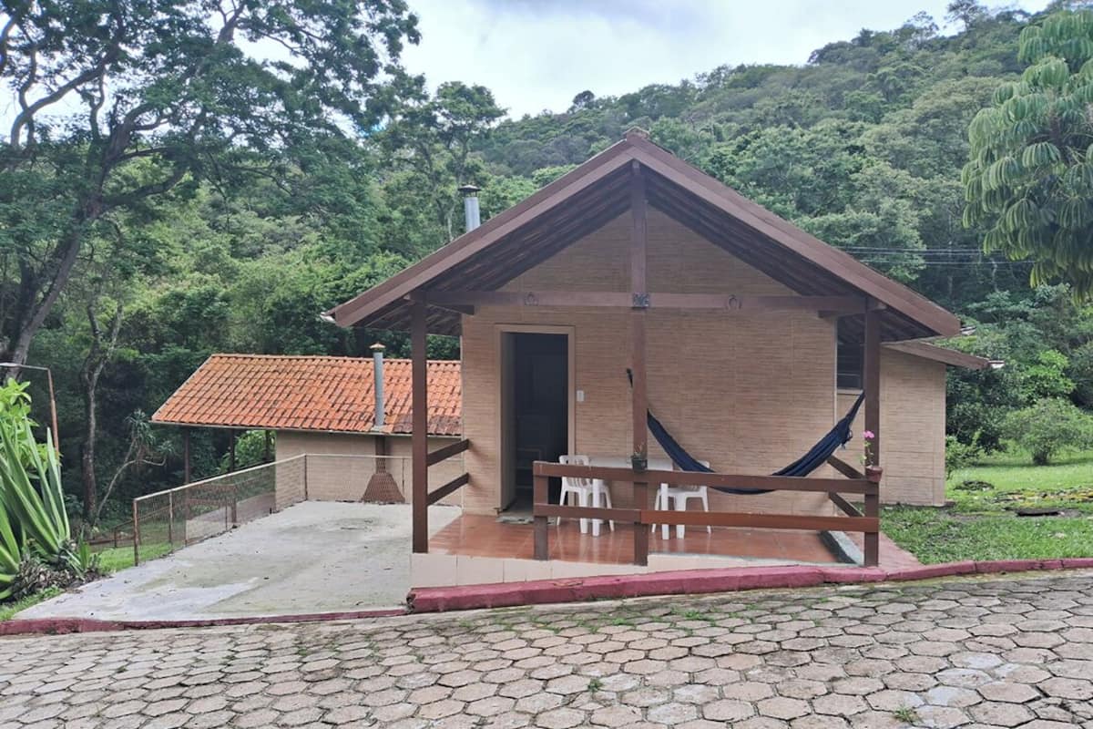 A small brick building with a tiled roof, a wooden porch, and a hammock.