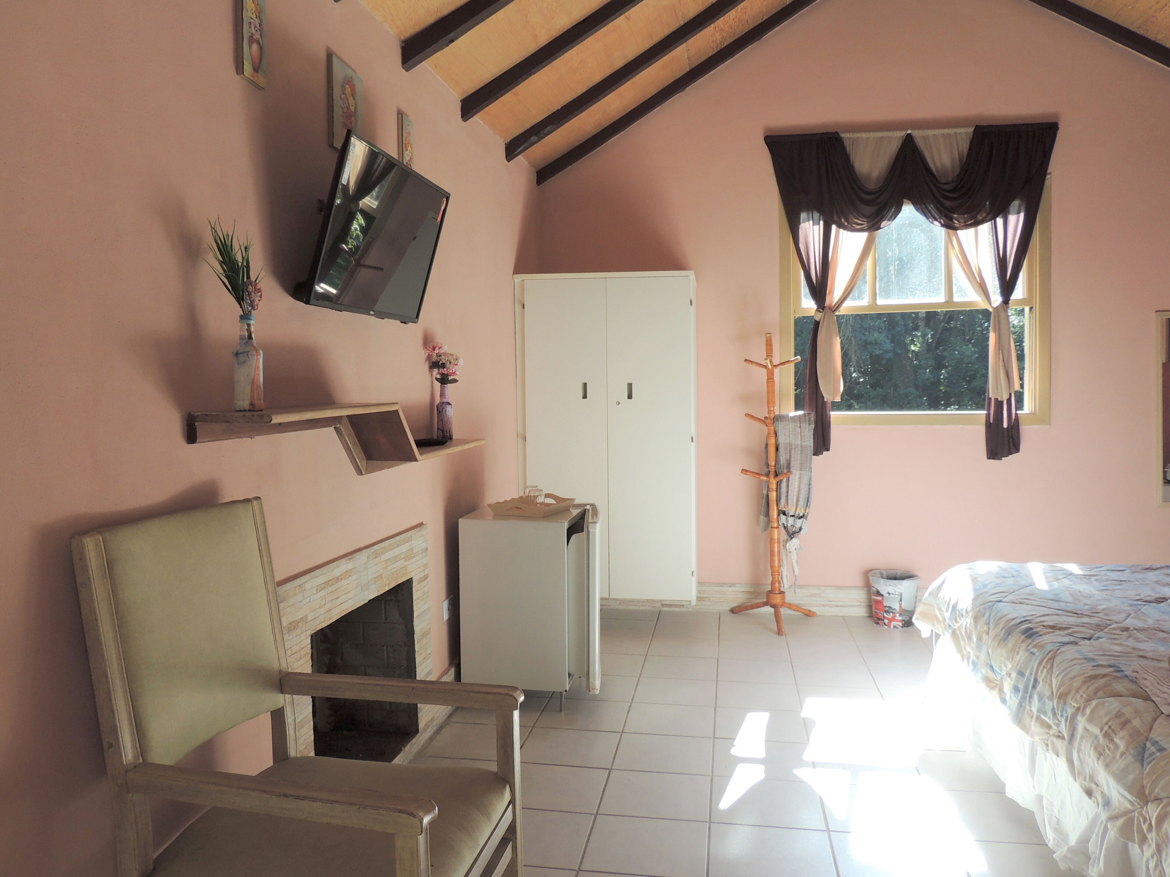 Ein Schlafzimmer mit einem Bett, einem Sessel, einem an der Wand befestigten Fernseher, einem Kleiderschrank und einem Fenster mit Vorhängen.